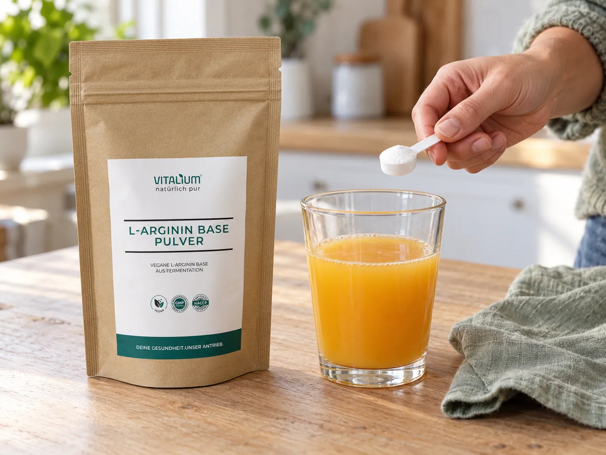 L-Arginin Base Pulver Beutel, daneben ein Messlöffel mit Pulver über einem Glas Orangensaft