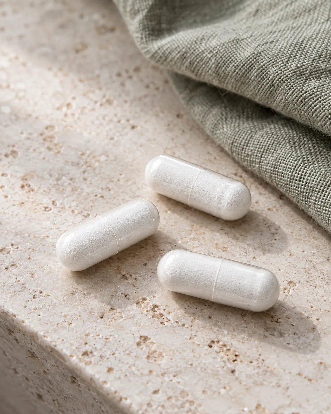 Drei weiße Kapseln des Magnesium 4-fach Komplexes auf hellem Naturstein
